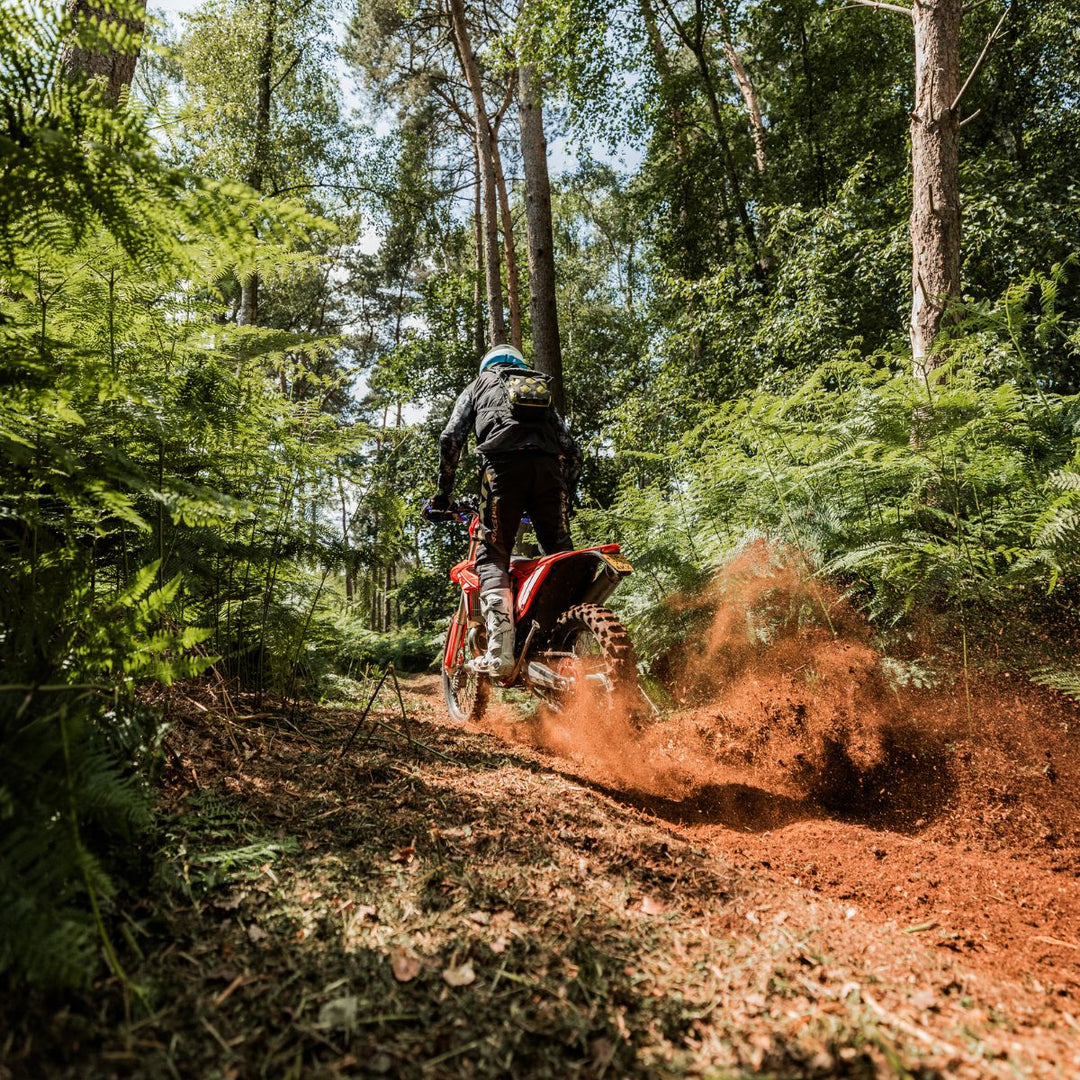 Motorcyclist riding through ancient woodland trails with red dirt roost at Loseley Estate