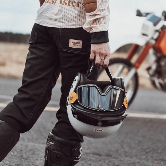 Wildust Sisters Cargo Overland Trousers – back view of female rider holding helmet, showing pocket badge detail and reverse of motocross top