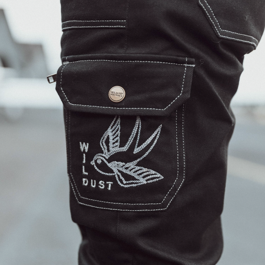 Wildust Sisters Cargo Overland Trousers – close-up of silver embroidery on black pocket with contrast white stitching and Wildust button detail