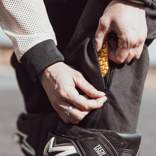 Wildust Sisters Cargo Overland Trousers – close-up of female rider zipping up protective pad insert in black moto trousers