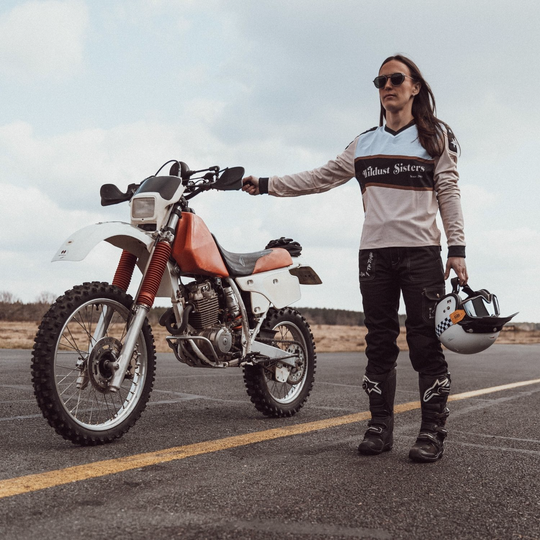 Wildust Sisters Cargo Overland Trousers – female rider on runway with dirt bike and helmet wearing black cargo trousers and wildust sisters motocross top