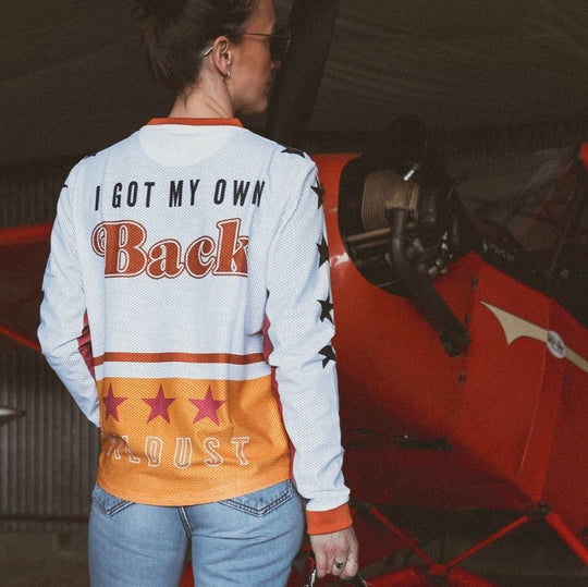 Model back view standing in front of vintage plane wearing Wildust Sisters Jersey Cross – Woman Racer top