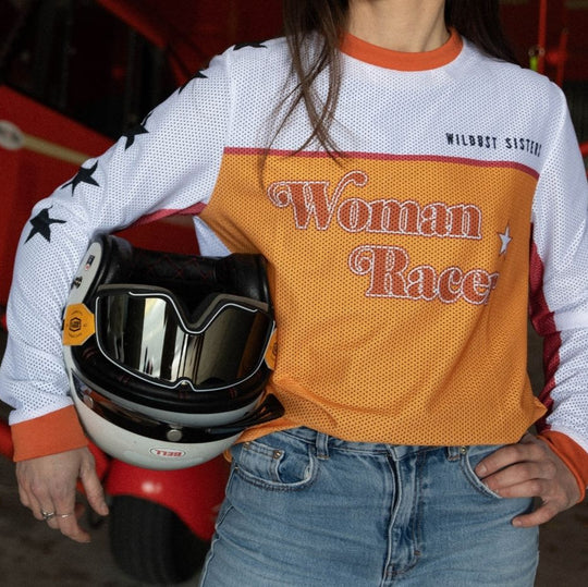Model front view holding motorcycle helmet and goggles wearing Wildust Sisters Jersey Cross – Woman Racer top