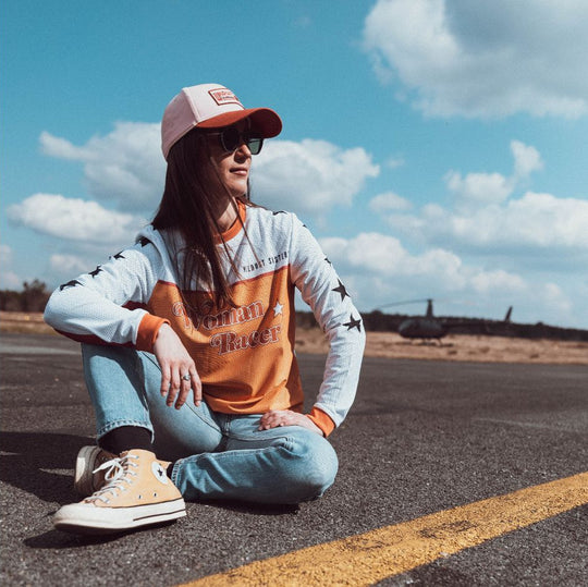 Model sat on tarmac road wearing front Model seated on tarmac road wearing Wildust Sisters Jersey Cross – Woman Racer top, front view