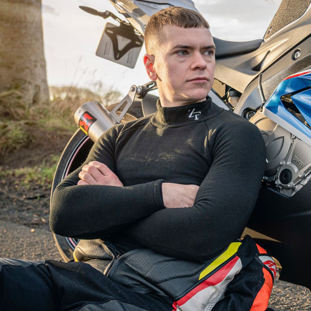 Motorcycle rider wearing Zerofit thermal baselayer leaning against BMW sports bike during outdoor ride stop.