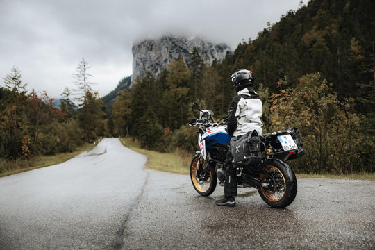 Boundless H2O ADV Footwear worn by a motorcyclist beside an adventure bike on a mountain road. 