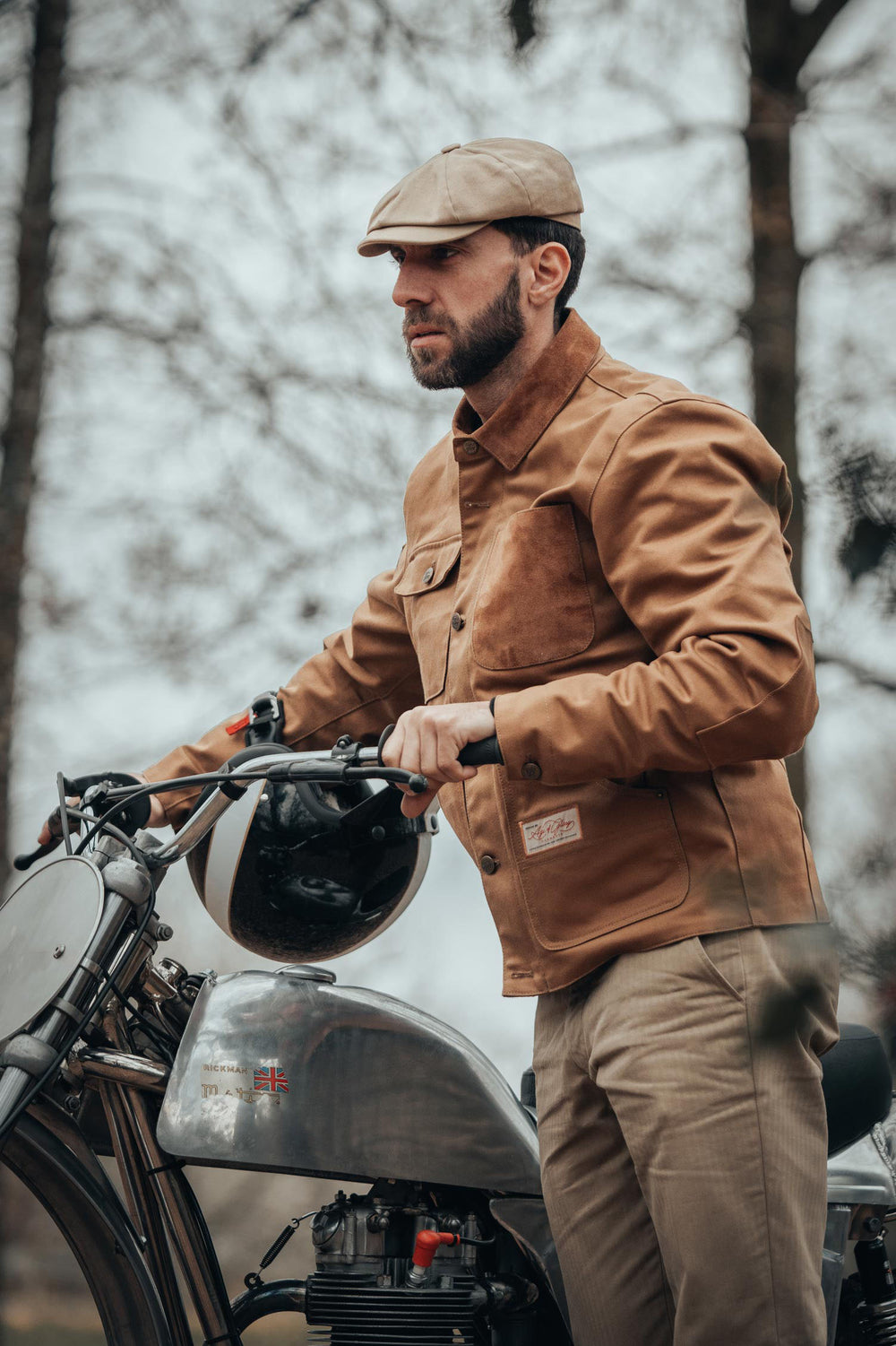 model-wearing-cap-age-of-glory-craftsman-motorcycle-jacket-camel-pushing-motorcycle