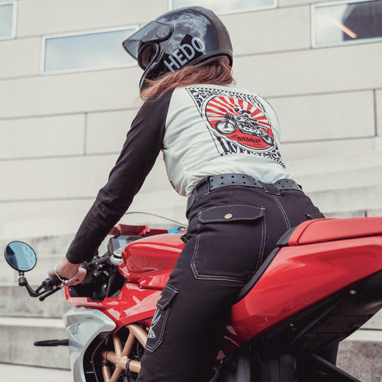 Rider on a red motorcycle wearing the Wildust Sisters Rebel Long Sleeve Tee with black sleeves and red-and-white back print, paired with black Wildust Overland trousers.