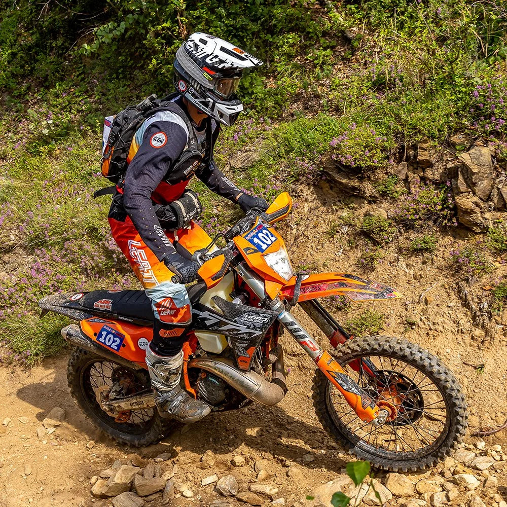 Chris Birch riding an orange dirt bike wearing the Kriega R3 Waistpack in an off-road rocky trail setting