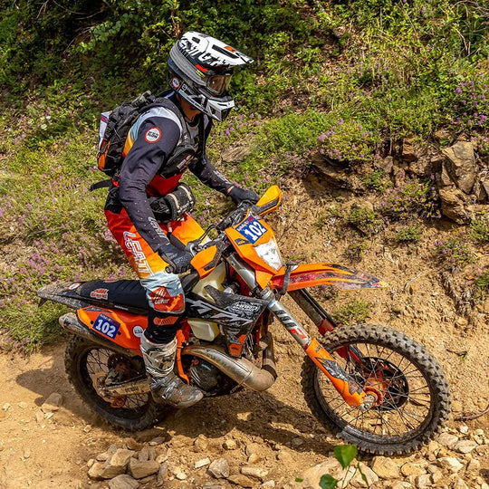 Chris Birch riding an orange dirt bike wearing the Kriega R3 Waistpack in an off-road rocky trail setting