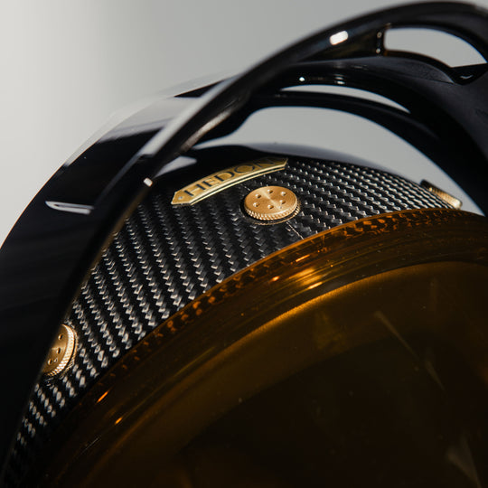Close-up detail of the Hedon Psilo Explorer Helmet – Commander with the tinted visor closed, highlighting the carbon fibre shell, Hedon badge, gold hardware, and Explorer peak.
