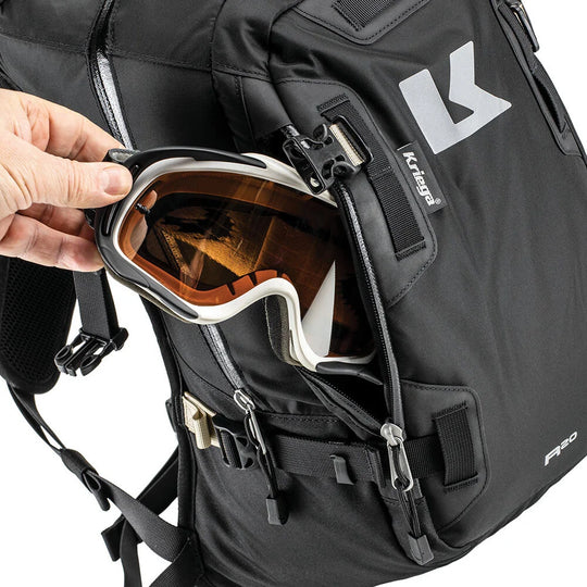 Black backpack with a hand placing goggles into an open pocket, featuring the Kriega brand.