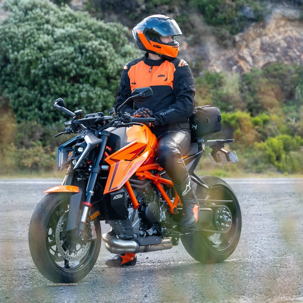 Kriega US-20 Drypack mounted on an orange KTM motorcycle, rider on the road with greenery in the background