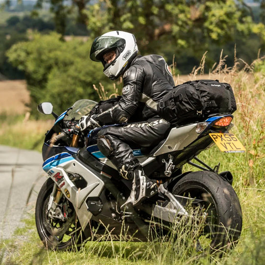 Suzuki motorcycle fitted with Kriega US-20 and US-10 Drypack luggage, parked roadside in natural setting with rider in leathers