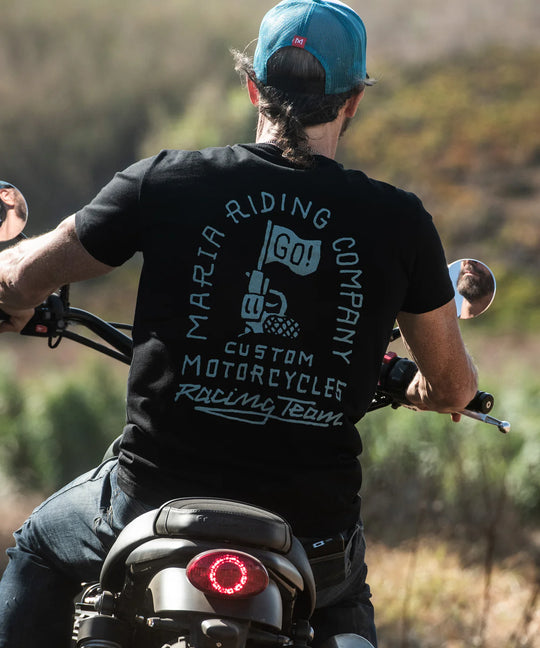 Person riding a motorcycle wearing a black t-shirt with text and graphics.
