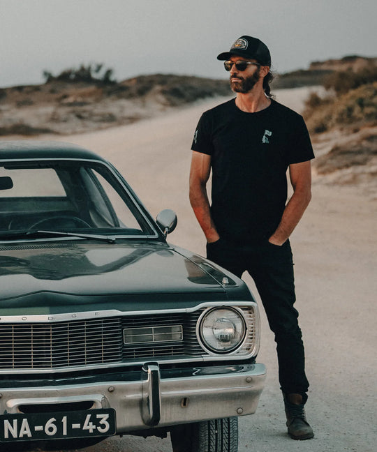 Man standing next to a vintage car on a desert road