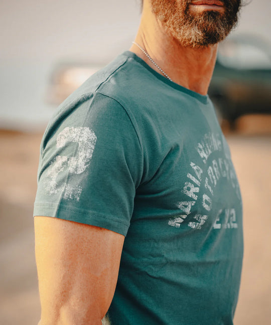 Man wearing a green t-shirt with text and graphics, standing outdoors.
