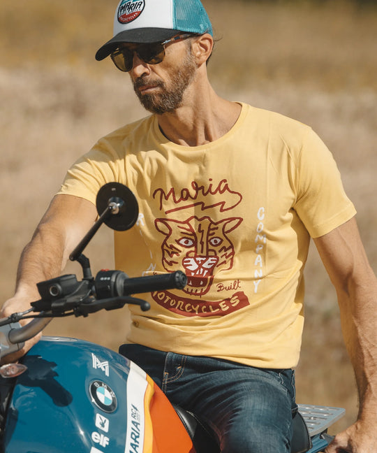Man wearing a yellow t-shirt with a tiger graphic and text, sitting on a motorcycle.