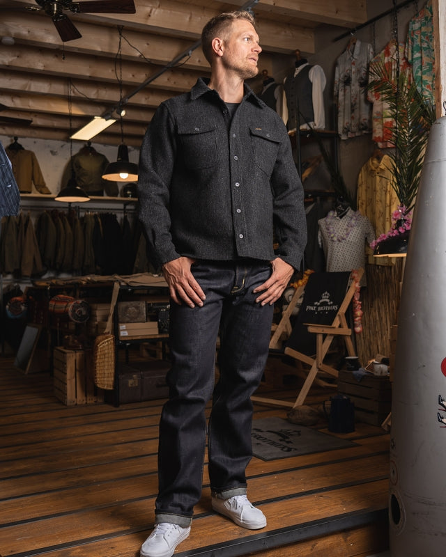 Male model wearing the Pike Brothers 1943 CPO Shirt Atlanta Grey and jeans in a workshop-style store