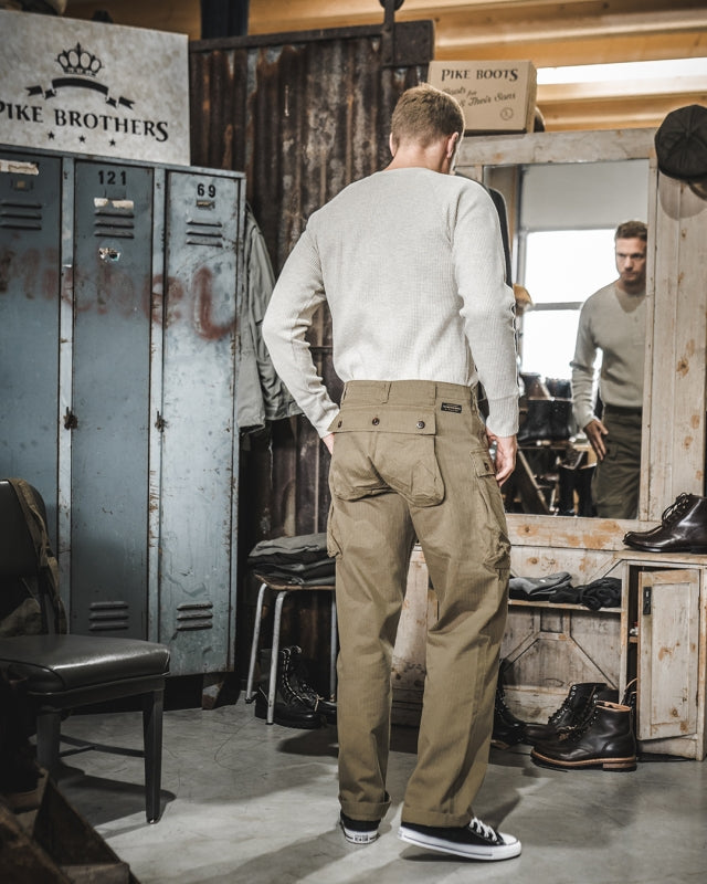 Back view of male model wearing Pike Brothers 1944 Monkey Pant in Olive – shop setting
