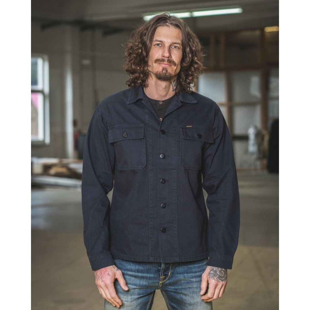 Pike Brothers 1962 OG-107 shirt navy men’s lifestyle image worn with denim showing front fit in workshop setting