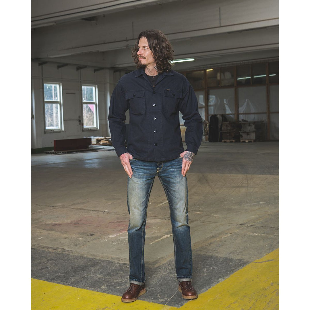 Pike Brothers 1962 OG-107 shirt navy full body lifestyle image worn with denim and boots showing overall fit in workshop setting