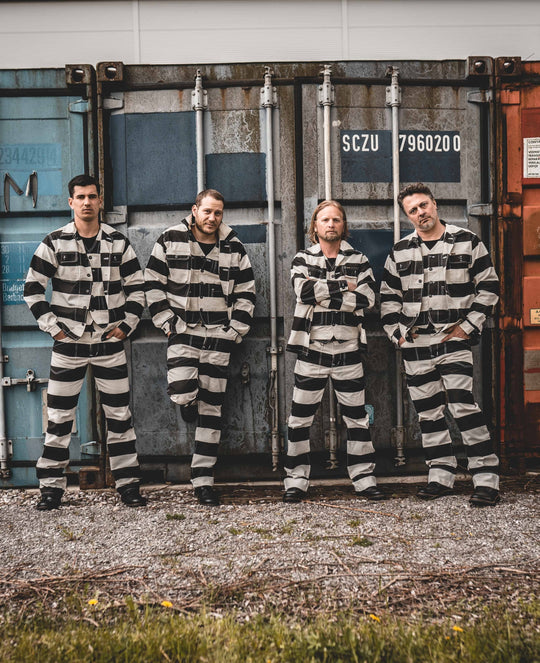 Four models wearing full Pike Brothers Alcatraz outfits – striped shirts, vests, and trousers – standing in front of shipping containers