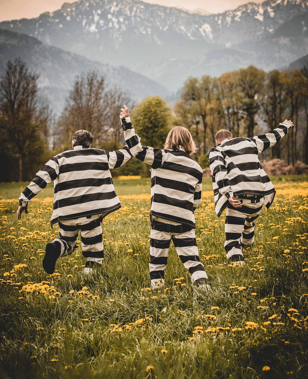 Back view of three models wearing Pike Brothers Alcatraz striped shirts and trousers, standing in a summer meadow with mountains in the background
