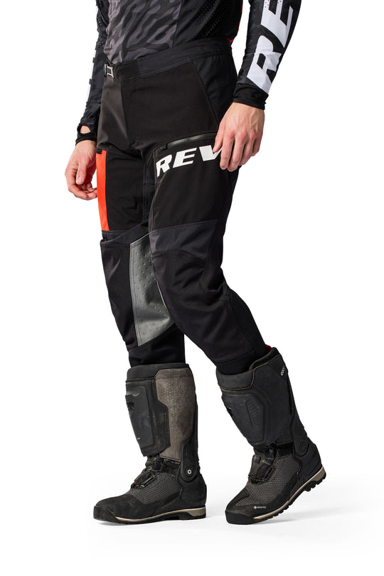 Model wearing REV’IT! Lejano Motorcycle Trousers in black and red, front three-quarter view.
