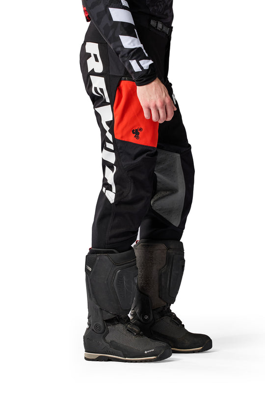 Model wearing REV’IT! Lejano Motorcycle Trousers in black and red, side view.
