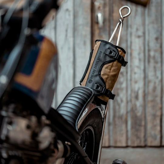 Roland Sands Design x Kriega Roam Tool Roll Ranger in brown mounted to motorcycle frame with wooden wall background
