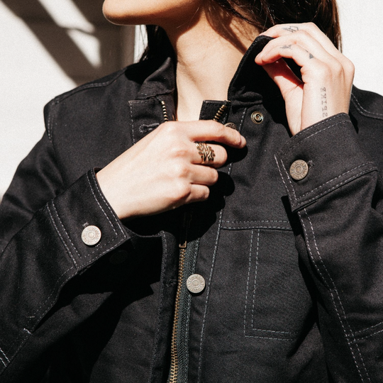 Close-up of female rider adjusting button on Wildust Sisters Pioneer Jacket in Black, showing contrast stitching
