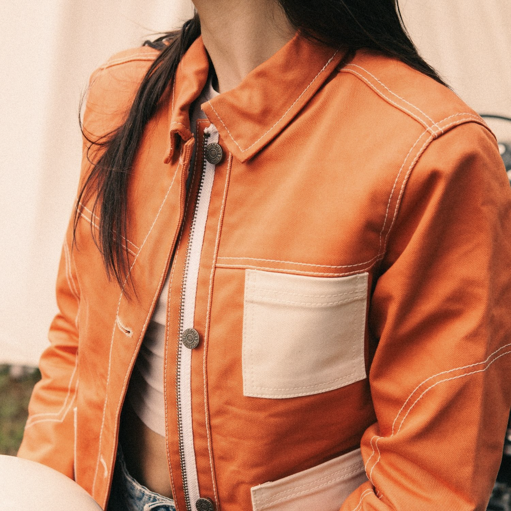 Close-up of female rider wearing Wildust Pioneer Jacket in Orange showing ivory pockets, contrast stitching, and buttons