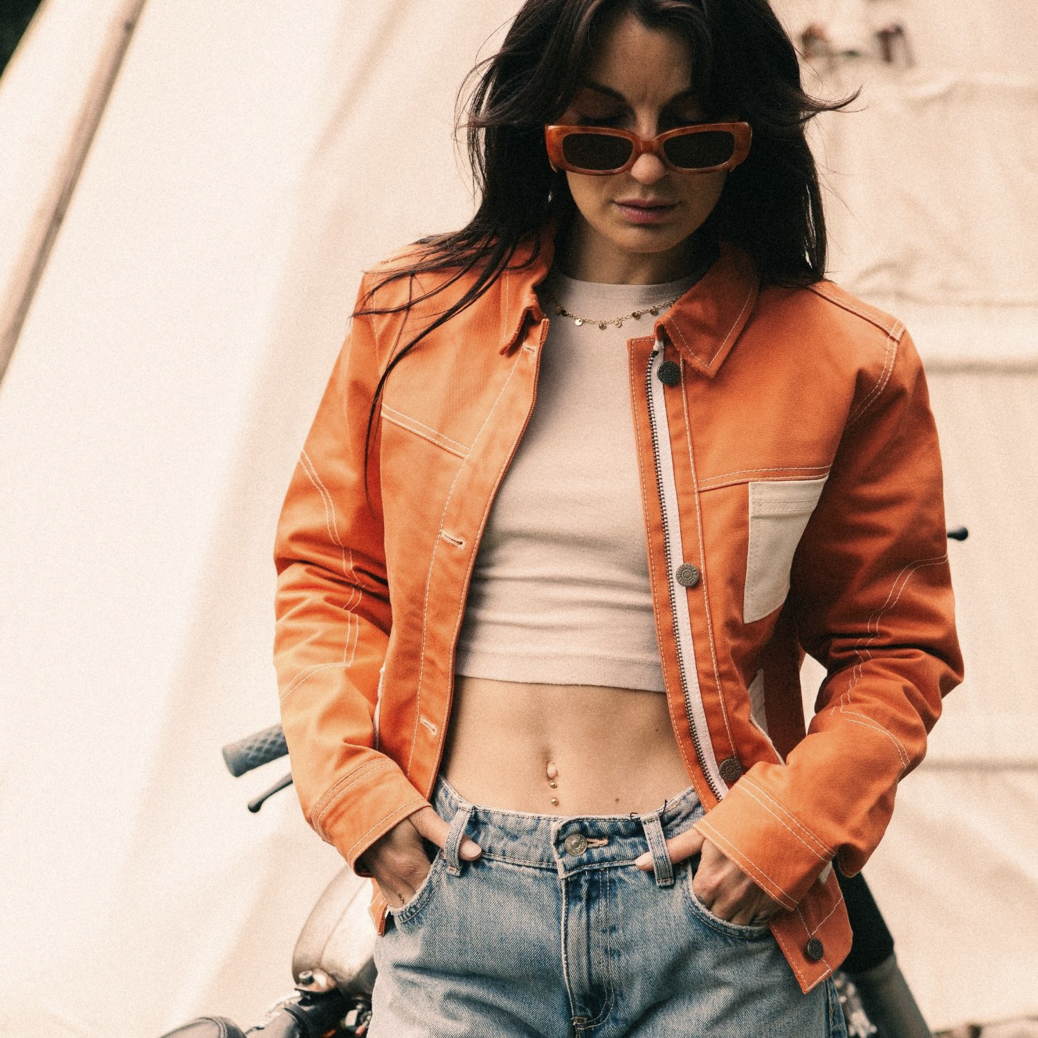 Female rider wearing Wildust Sisters Pioneer Jacket in Orange, unzipped with jeans and sunglasses, front view