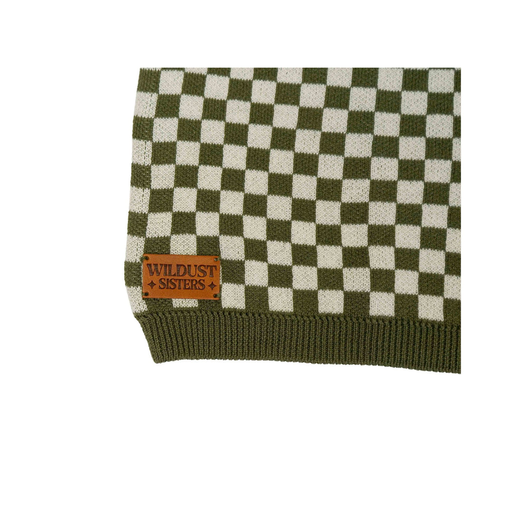 Close-up of the Wildust Sisters Vintage Racing Jumper in Khaki showing the signature leather brand patch and chequered cotton knit