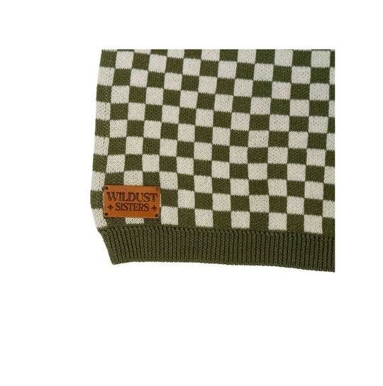 Close-up of the Wildust Sisters Vintage Racing Jumper in Khaki showing the signature leather brand patch and chequered cotton knit