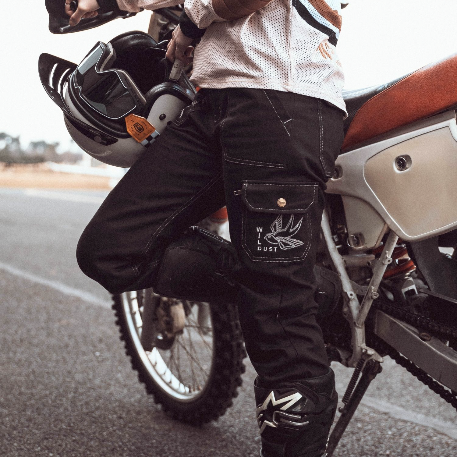 Wildust Sisters Cargo Overland Trousers – black protective moto pants worn by female rider standing next to motorcycle with helmet