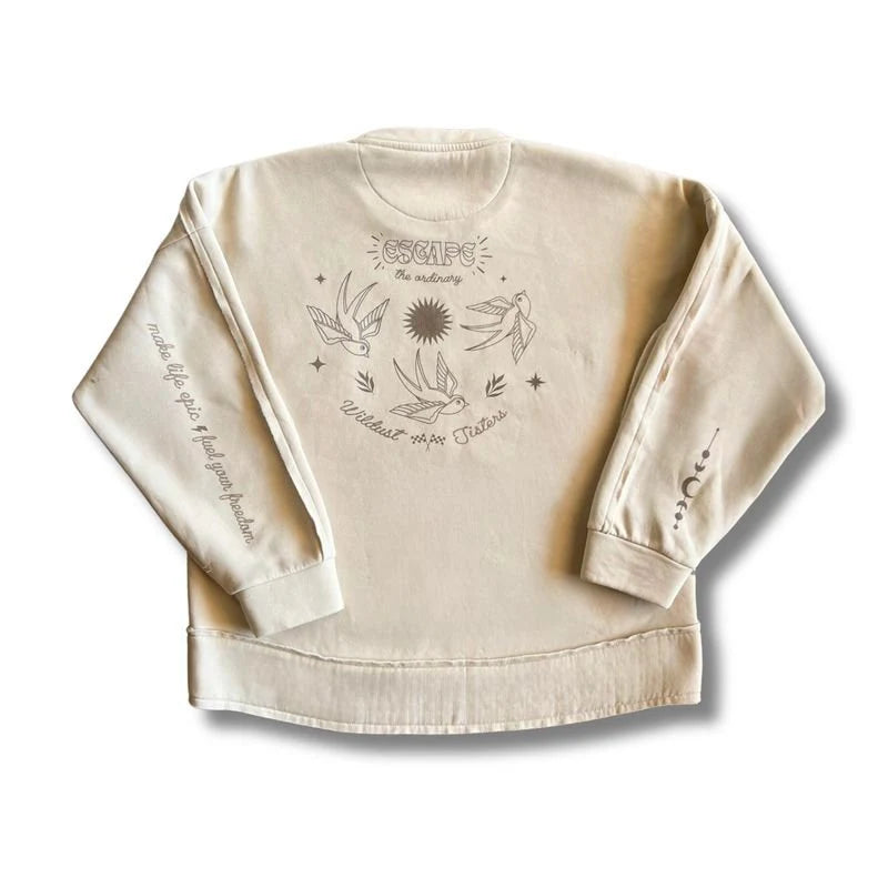 Wildust Sisters Escape Sweatshirt in ecru with “Escape the Ordinary” back print featuring swallows, sun and sleeve text, on white background.