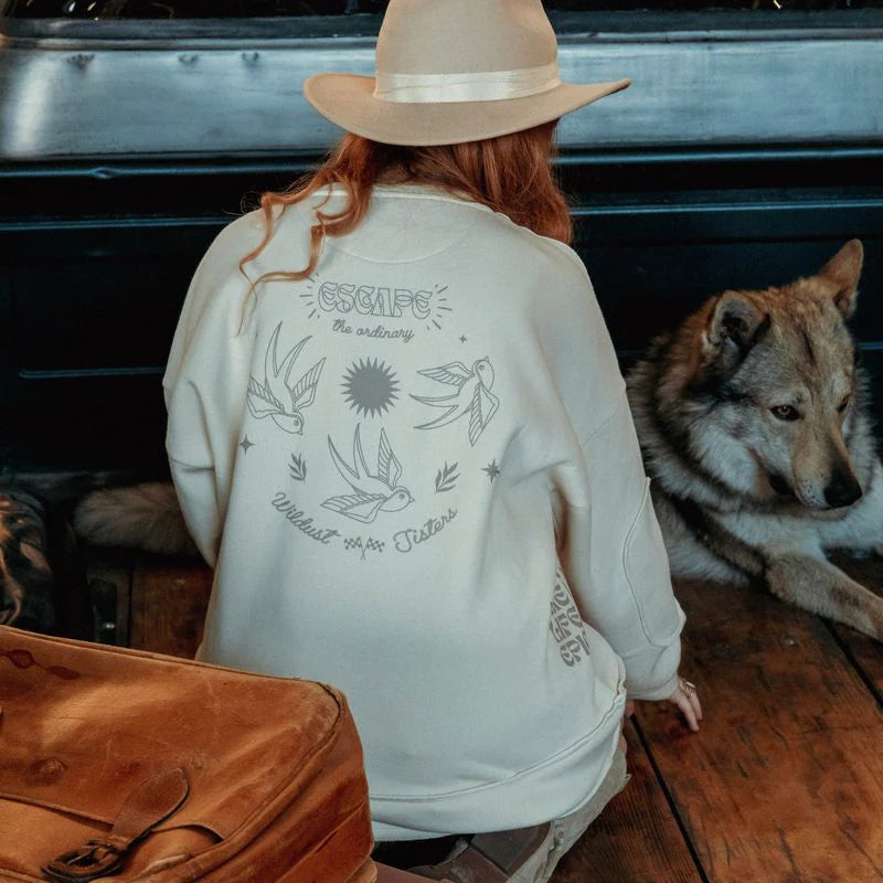 Model wearing the Wildust Sisters Escape Sweatshirt showing back print standing beside a wolf on wooden floor.