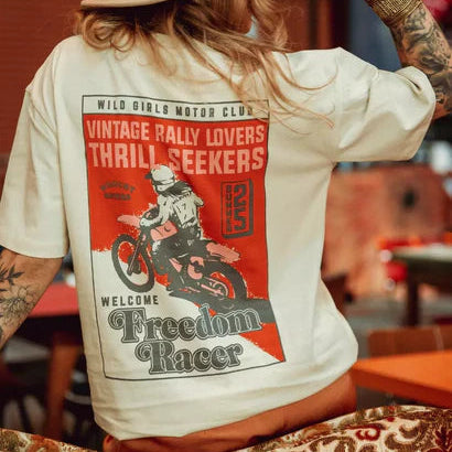Model in hat wearing Wildust Sisters Freedom Racer T-shirt, showing large back graphic while seated.