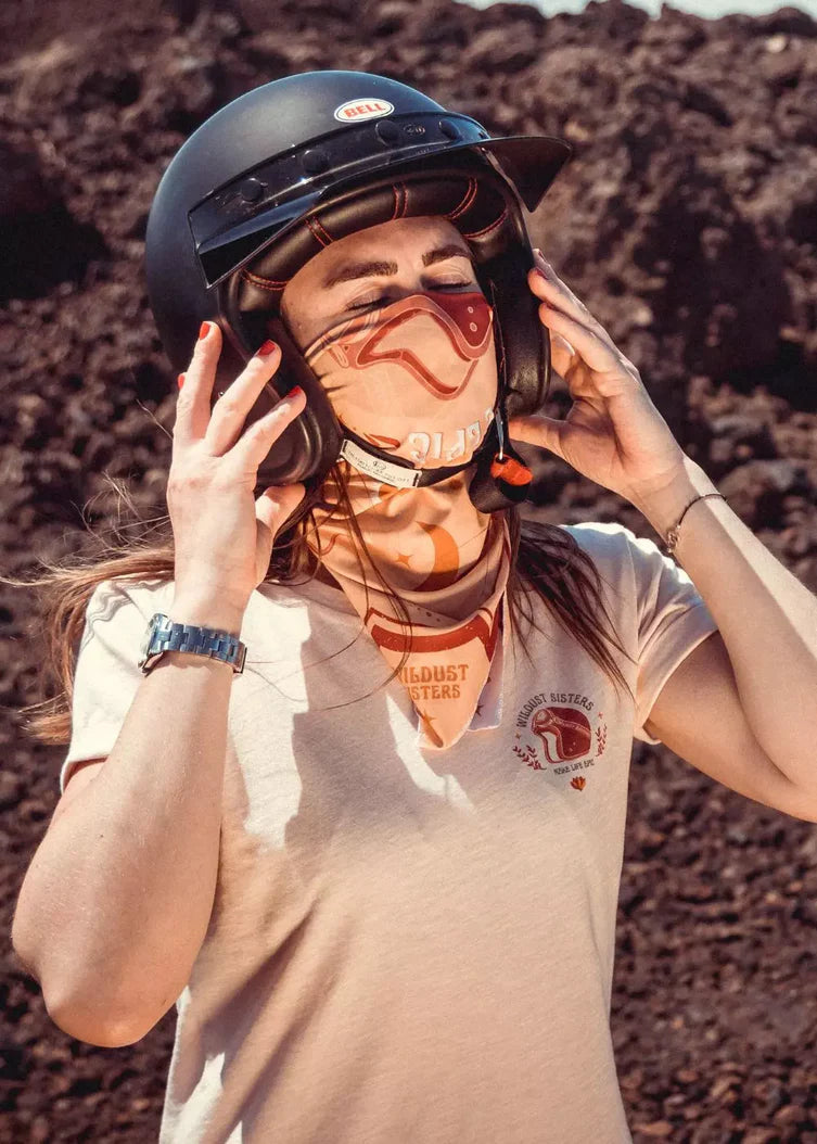 Close-up of a rider adjusting a helmet and wearing the Wildust Sisters “Make Life Epic” scarf in yellow, red, and ecru, photographed outdoors.