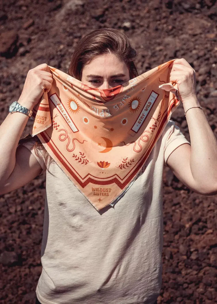 Rider holding the Wildust Sisters “Make Life Epic” scarf showing its reversible yellow, red, and ecru design, photographed outdoors.