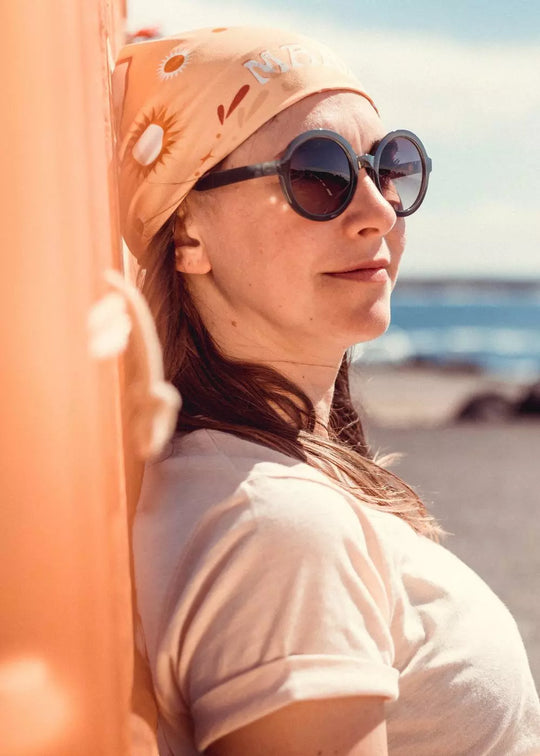 Rider wearing sunglasses and the Wildust Sisters “Make Life Epic” scarf as a headscarf, photographed outdoors near the coast.