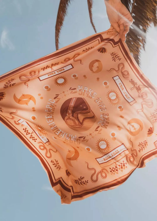 Wildust Sisters “Make Life Epic” scarf in yellow, red, and ecru held up outdoors against a blue sky, showing its reversible design and artwork details.